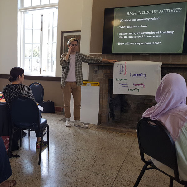 man stands before group of people giving a presentation