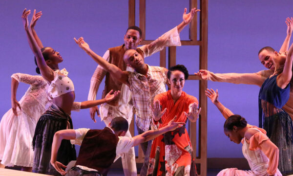 A group of dancers perform against a blue background