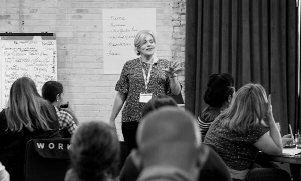 Woman stands before class of adults, photo black and white