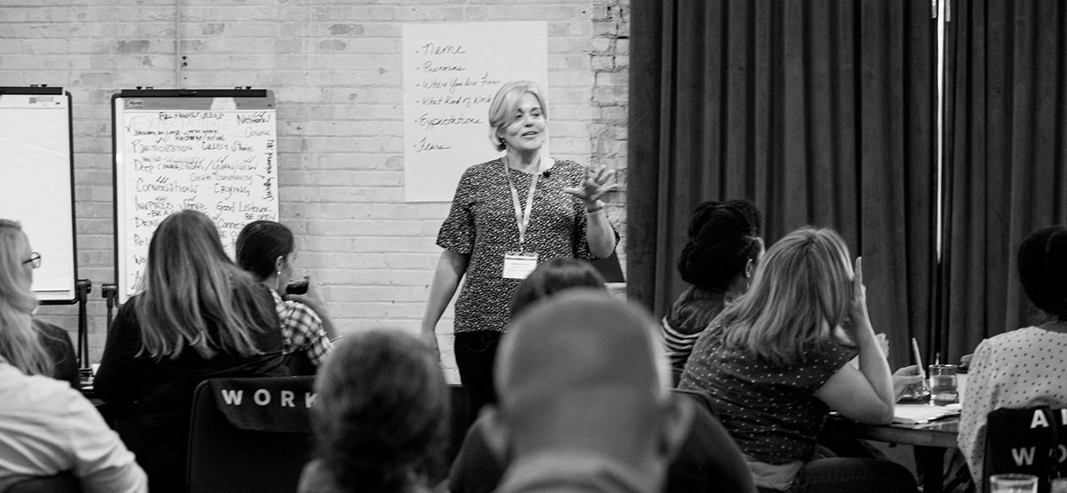 Woman stands before class of adults, photo black and white