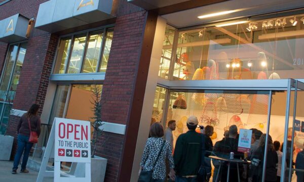 people walk into an illuminated gallery in the early evening