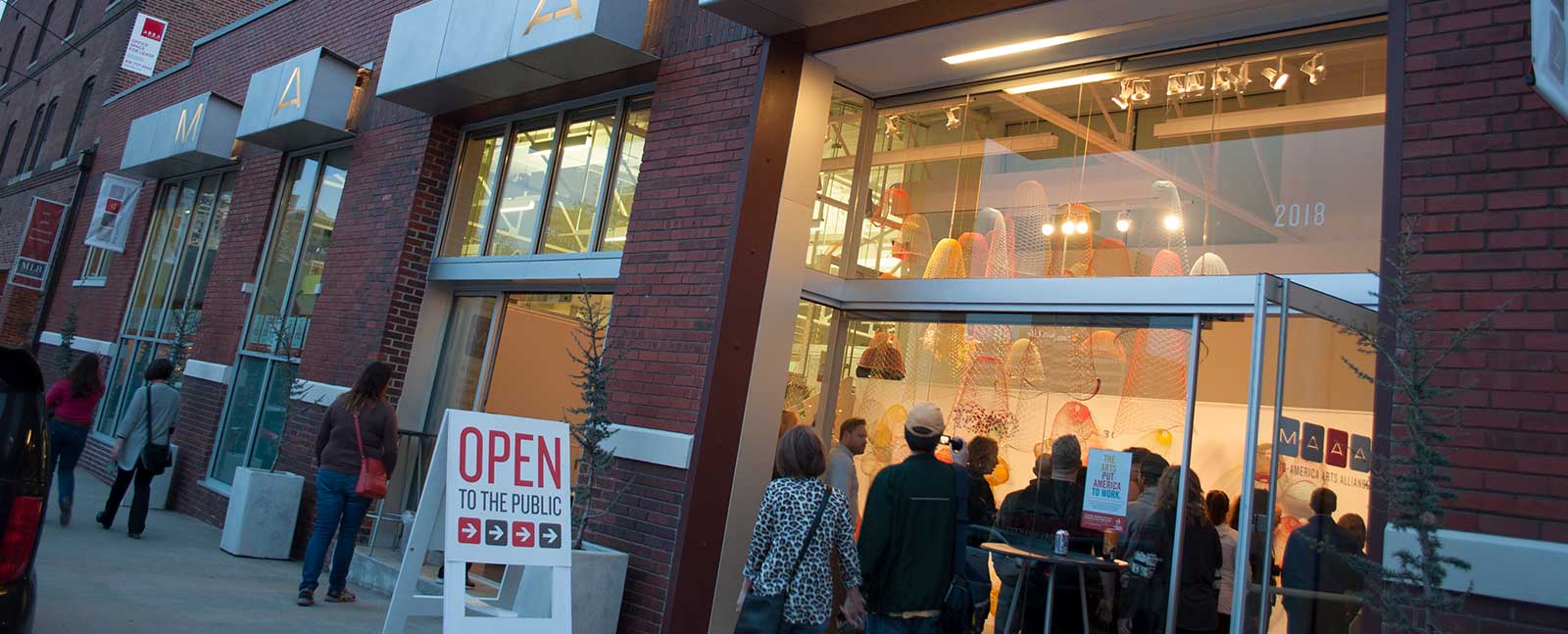 people walk into an illuminated gallery in the early evening