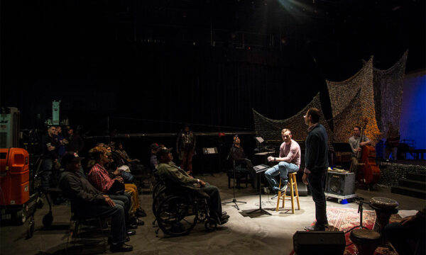 man onstage, seated on a stool in a spotlight