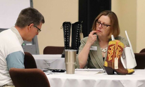 two people in conversation, woman at right has hand pointed to her face as if she's thinking