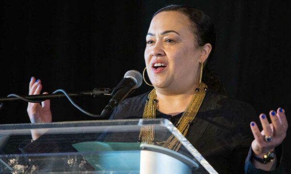 woman talks at podium with arms outstretched