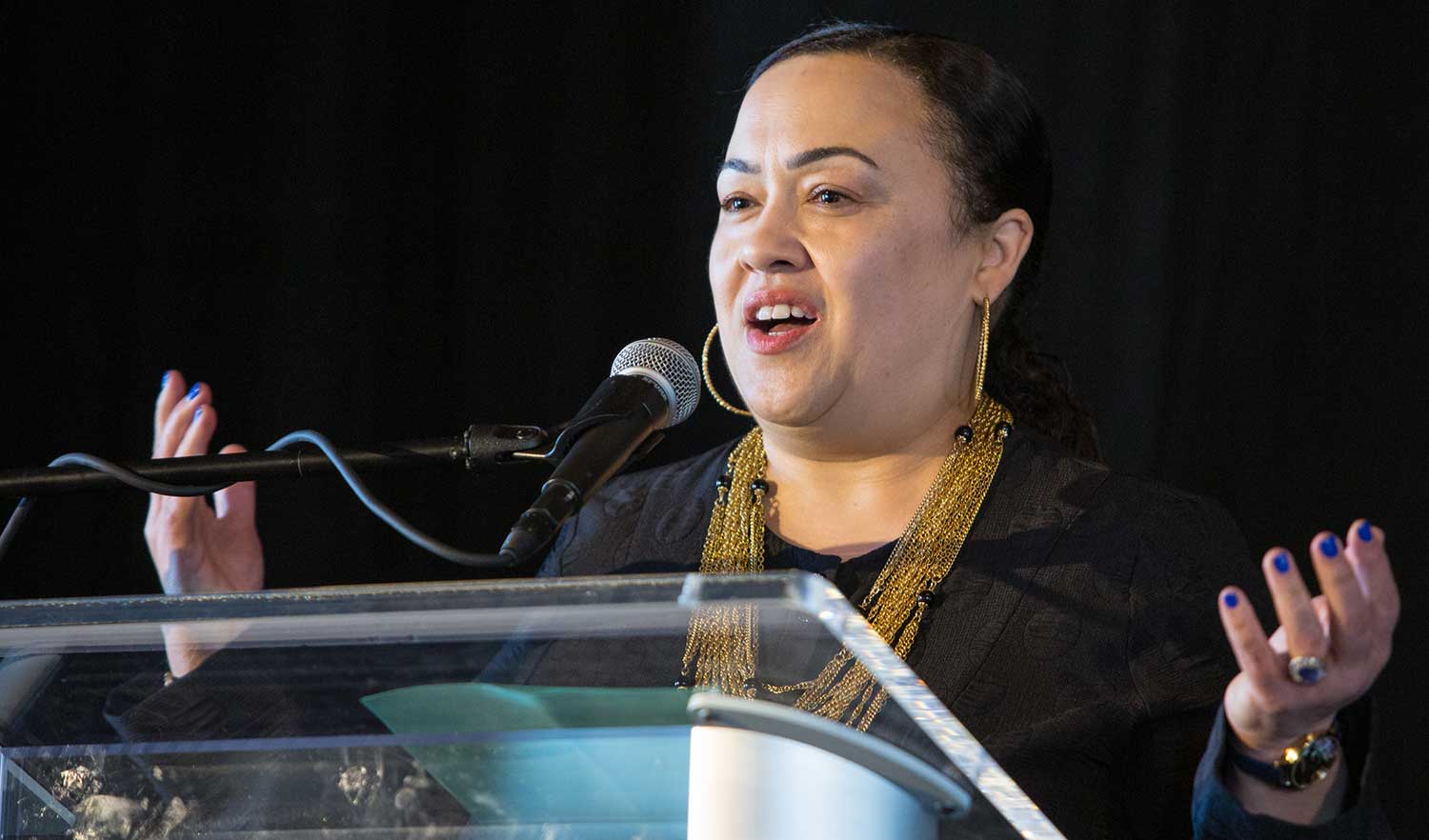 woman talks at podium with arms outstretched