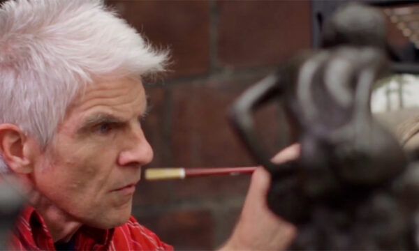 A man with white hair works on a sculpture