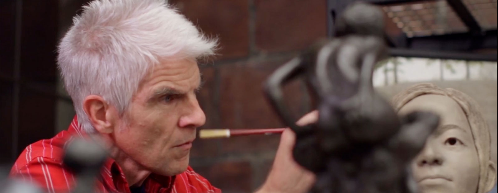 A man with white hair works on a sculpture