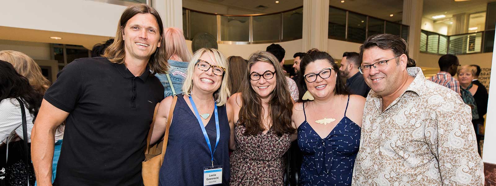 a group of five people pose at a crowded event