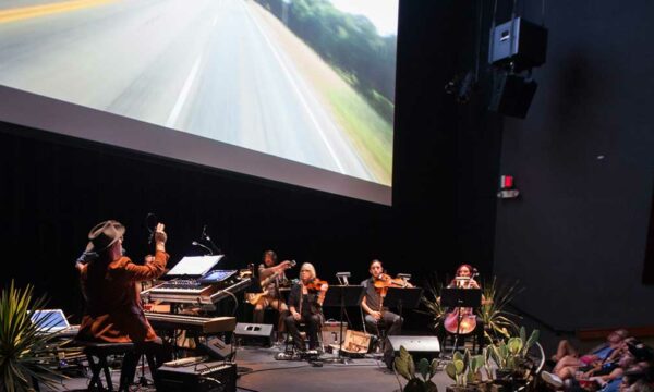 Classical musicians perform just below a screen with an image of an open road