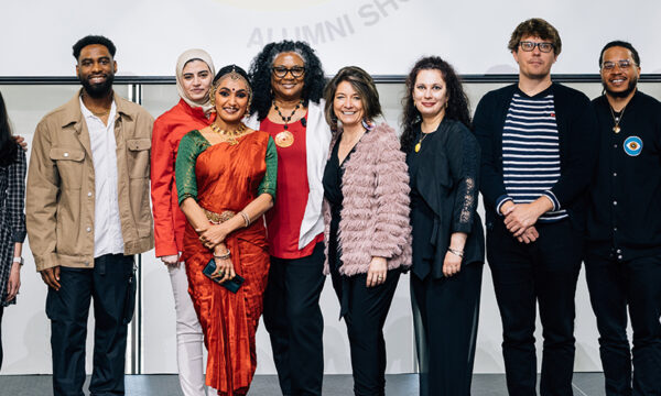 A group of people representing many different ages and ethnicities stand on a stage smiling for a group photo.