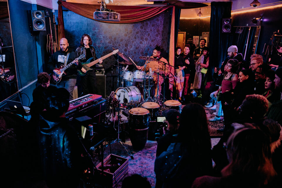 Large group of jazz musicians on a stage with dark purple curtains in the background.