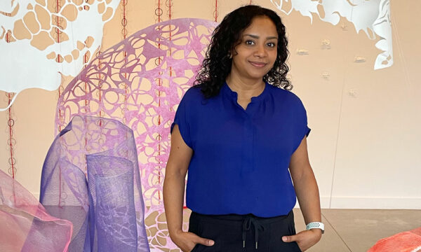 Artist Sukanya Mani in a blue shirt standing in her cut-paper installation at the M-AAA Culture Lab gallery.