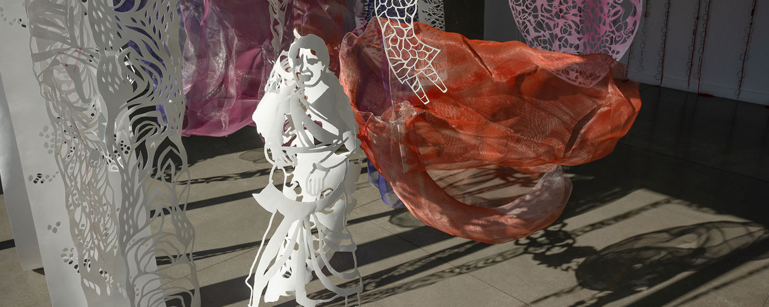 Cut paper detail featuring a woman with a background of a gallery with hanging orange and pink wire mesh sculptures.