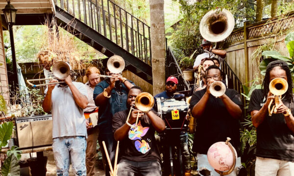 Jazz artists outdoors with all of their instruments in action: horns ready and covering their faces.