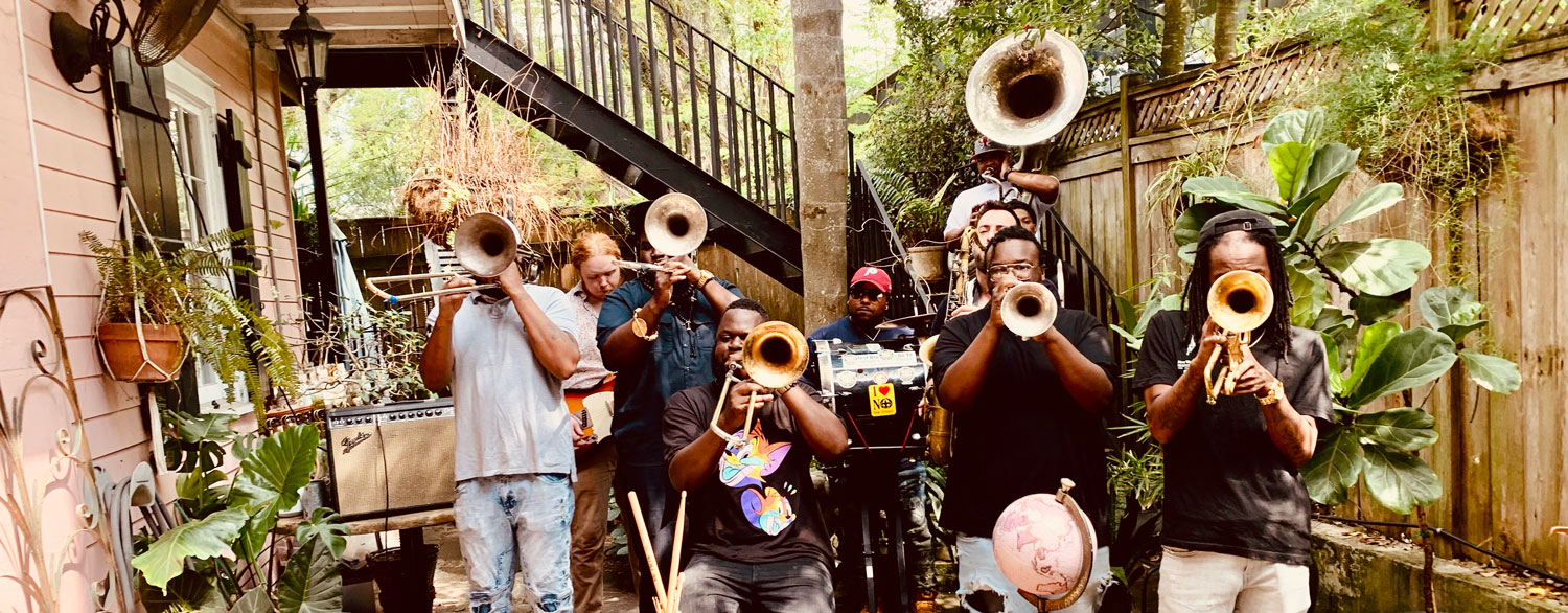 Jazz artists outdoors with all of their instruments in action: horns ready and covering their faces.