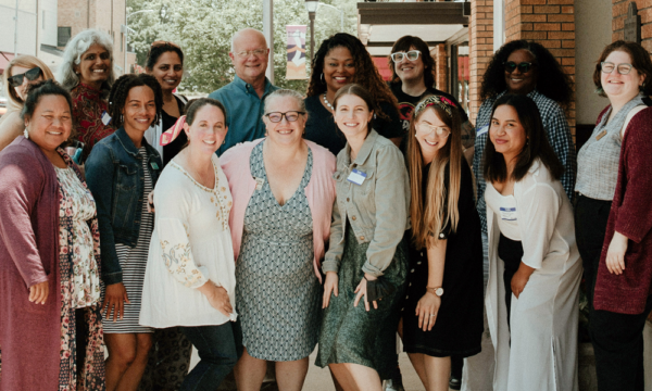 Group of fifteen people stand together smiling outdoors.