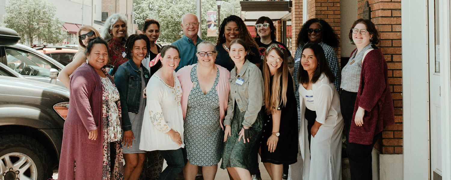 Group of fifteen people stand together smiling outdoors.