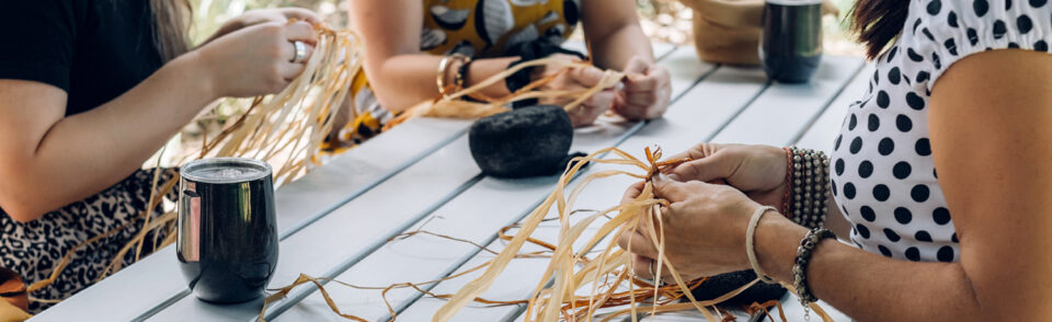 light-skinned women weave hay at a picnic table.