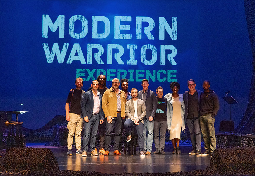 Group of people pose onstage with a background that says Modern Warrior Experience.