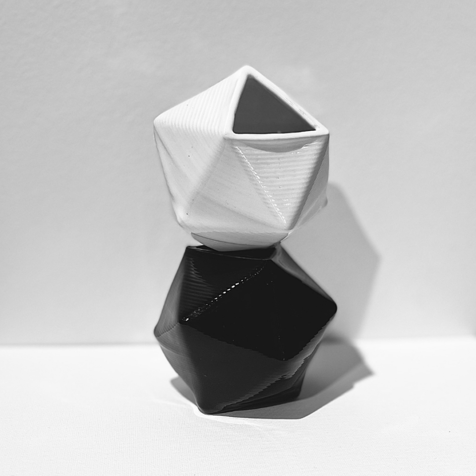 White geometric ceramic sculpture sits on top of a black geometric ceramic sculpture.