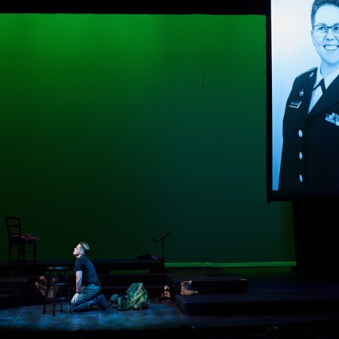 Man kneels onstage with a green backdrop.