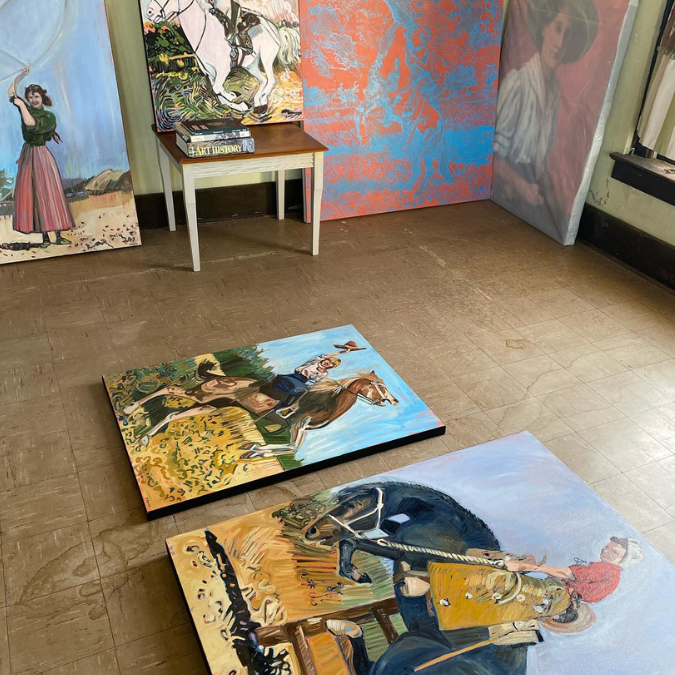 Large canvases of cowgirls on the floor and on walls in a studio.