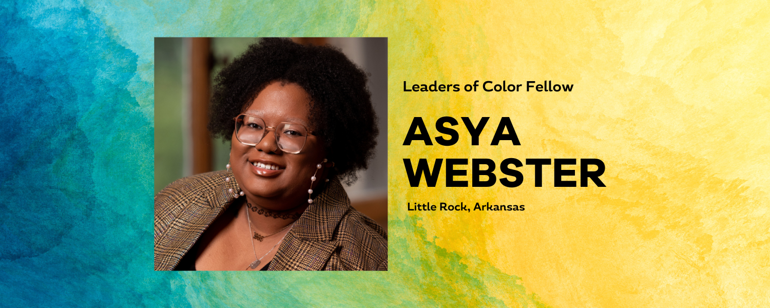 Female-presenting individual with medium dark skin and brown blazer with glasses smiles at camera in a headshot portrait. Background is a colorful blue green yellow painterly gradient with the name Asya Webster written.