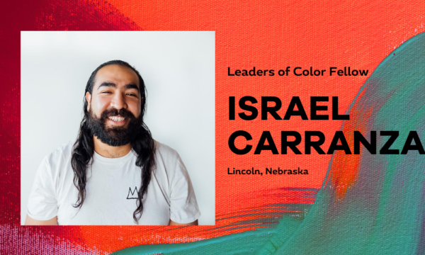 Male presenting individual with long dark hair smiles for a portrait with a white background and painterly red and green background surrounding that. Text states Israel Carranza.