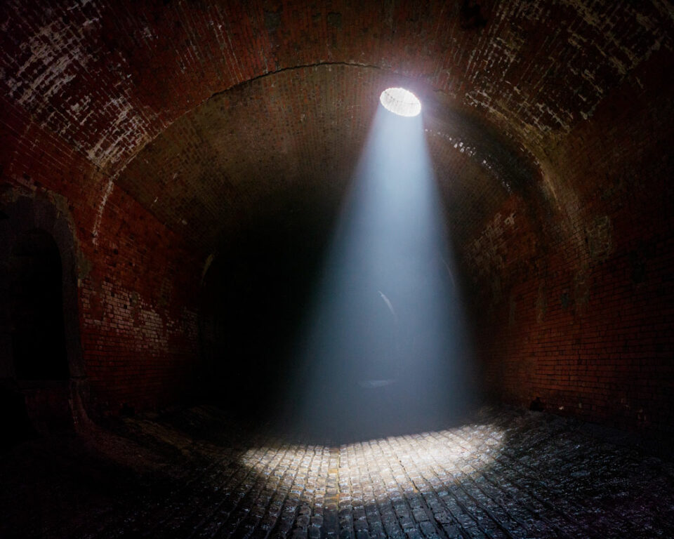 Daylight shines down into a dark sewer.