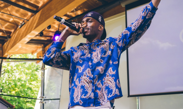 Man with blue printed shirt speaks into a microphone with his hand in air.