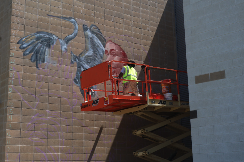 Mural artist on a large orange lift beginning to paint a mural.