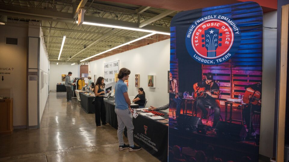 People speak at tables to conference attendees. One large standing sign in the front says, "music friendly community."