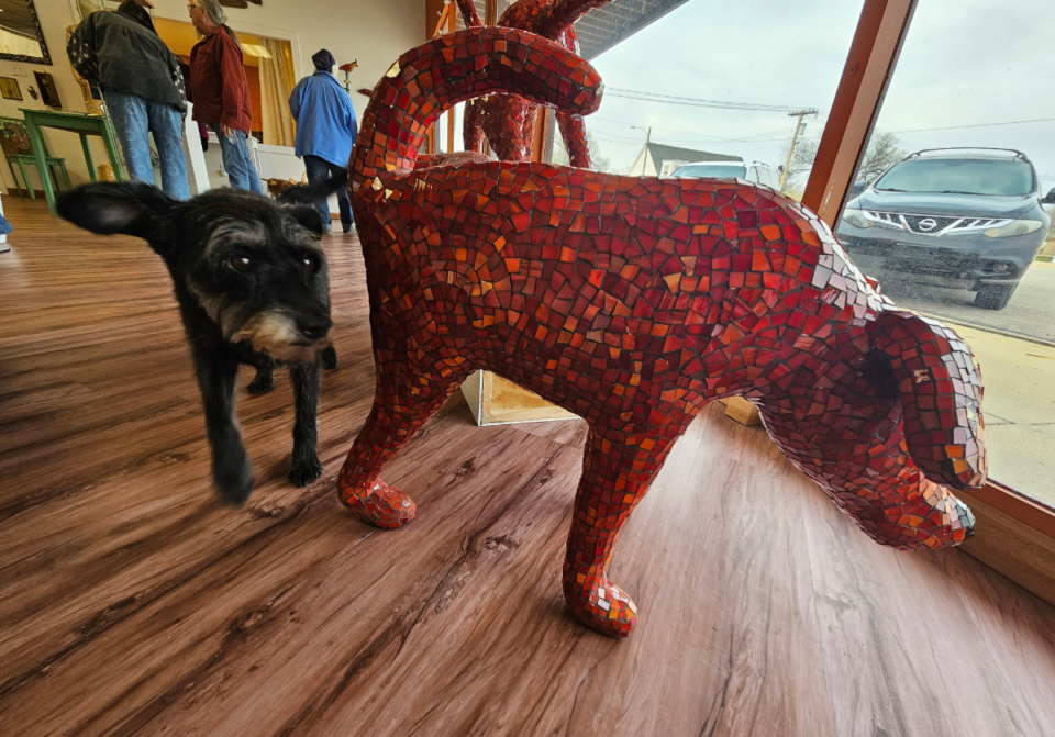 A red mosaic dog sculpture in a gallery window with a real dog standing with it.