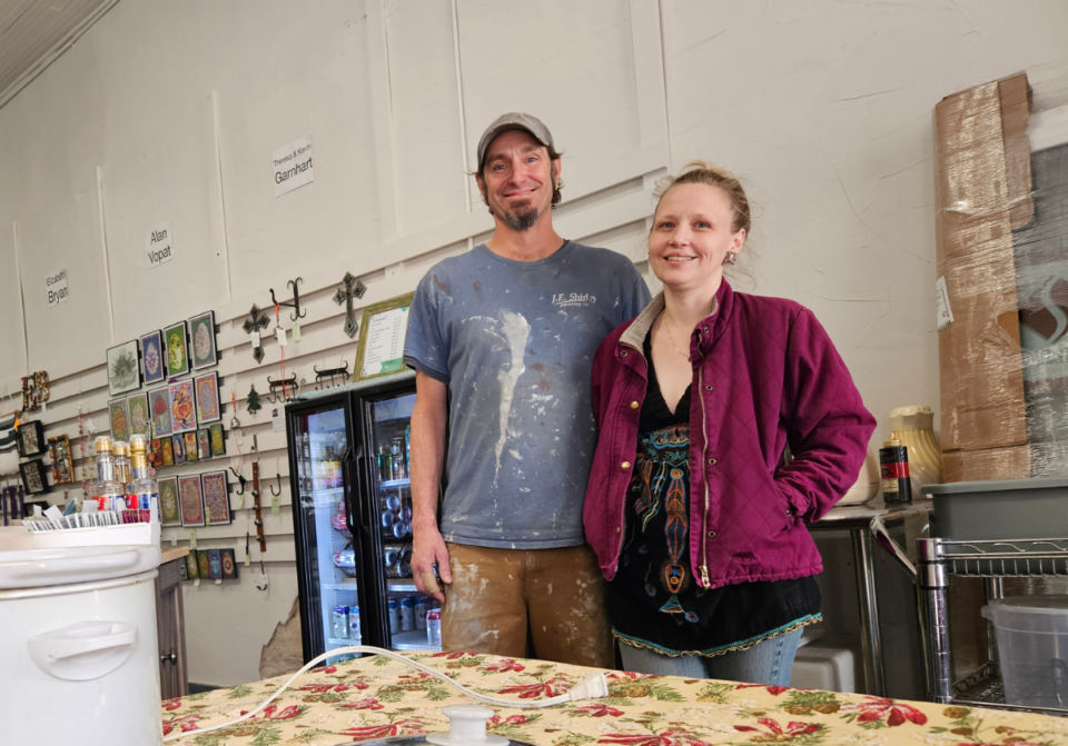 A smiling Caucasian man and woman stand in a large working art studio.