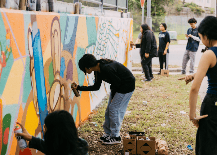 A group of people paint a mural using spraypaint.
