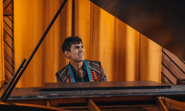 Man sits at a grand piano smiling.