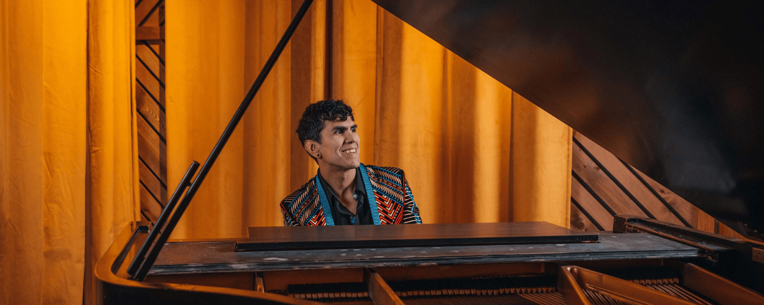 Man sits at a grand piano smiling.