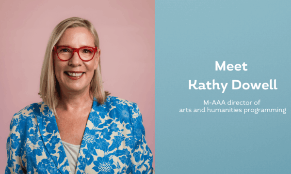 Kathy Dowell wears red glasses and a floral blue jacket in a headshot portrait.